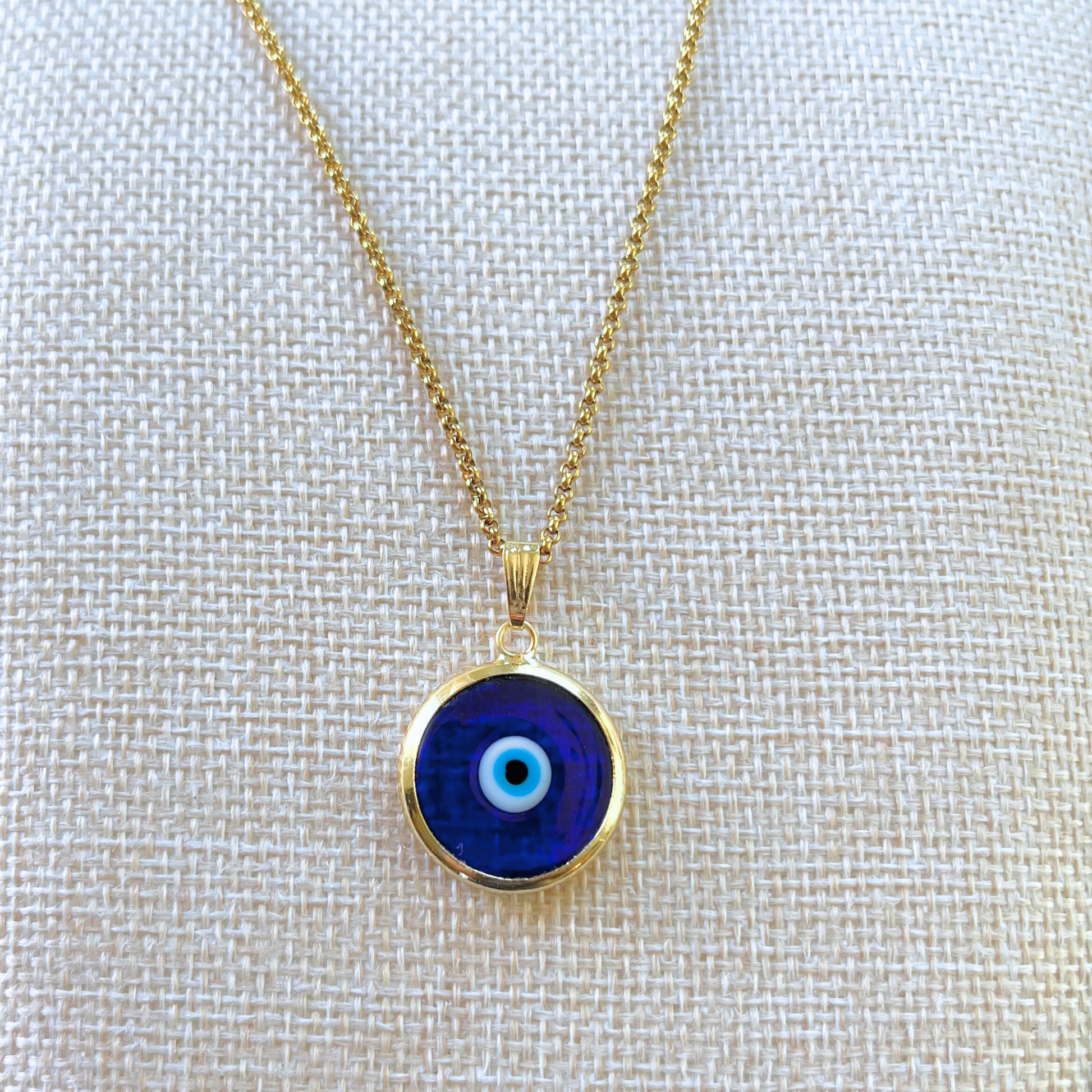 close-up frontal view of dark blue handmade turkish evil eye necklace modeled on beige bust. lampwork glass evil eye framed in gold-plated stainless steal with gold-plated stainless steel chain.