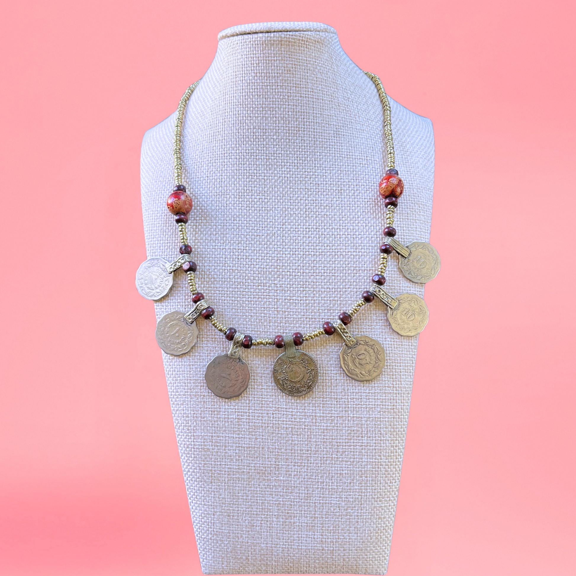 necklace modeled on a beige bust with a pink background. Necklace features turkish coins, metal beads, and wooden beads. view from the front