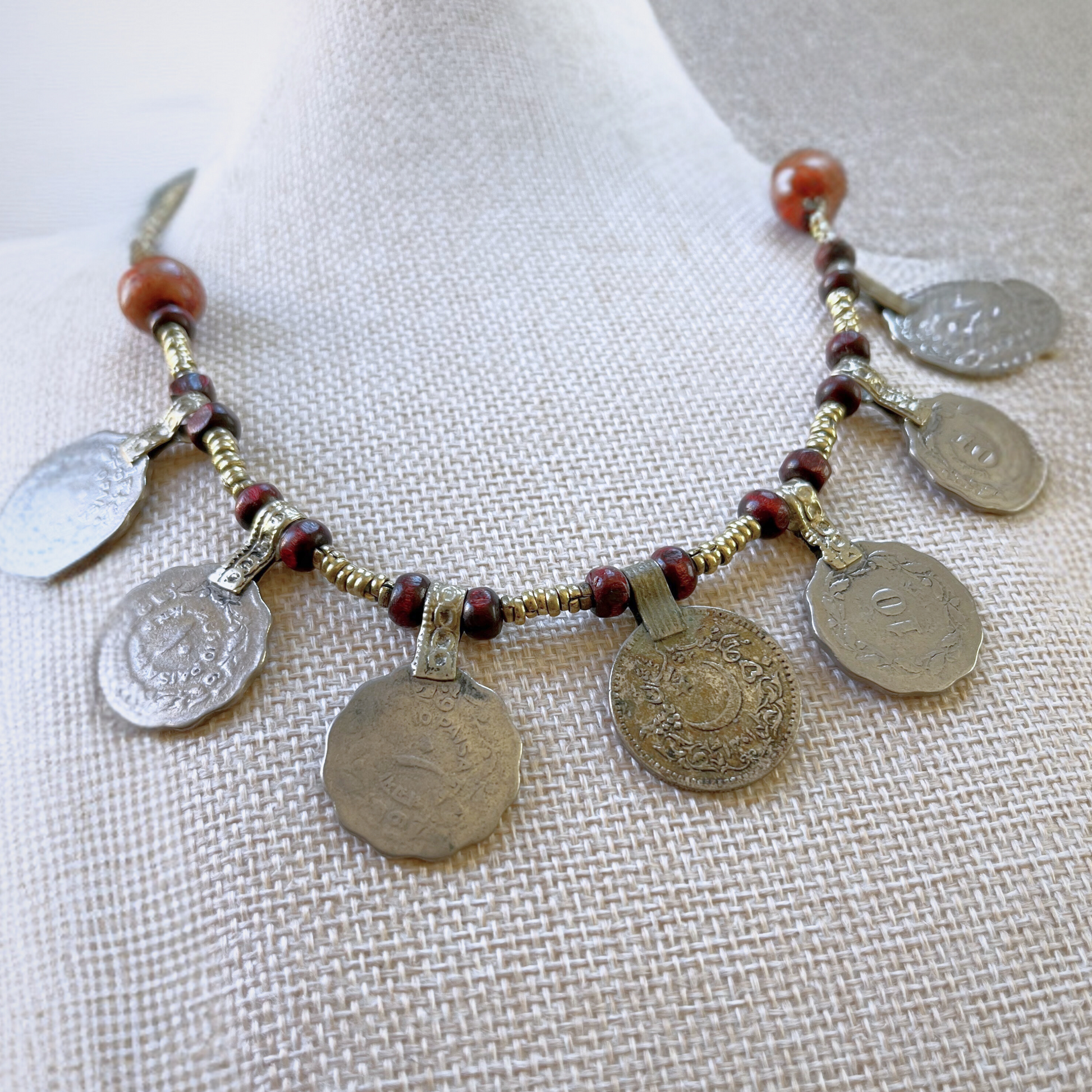 close-up view from above of a necklace modeled on a beige bust. Necklace features vintage turkish coins, metal beads, and wooden beads.