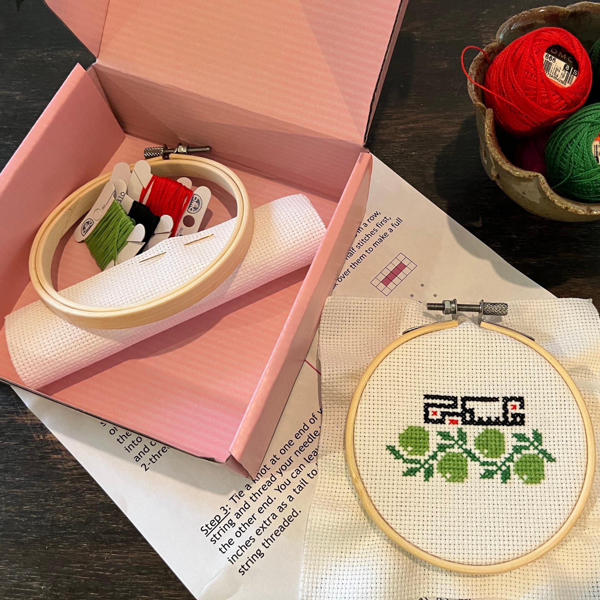 Inside view of olive branch and Palestinian tatreez kit box with tatreez instructions, embroidery thread, embroidery hoop, and aida cloth.