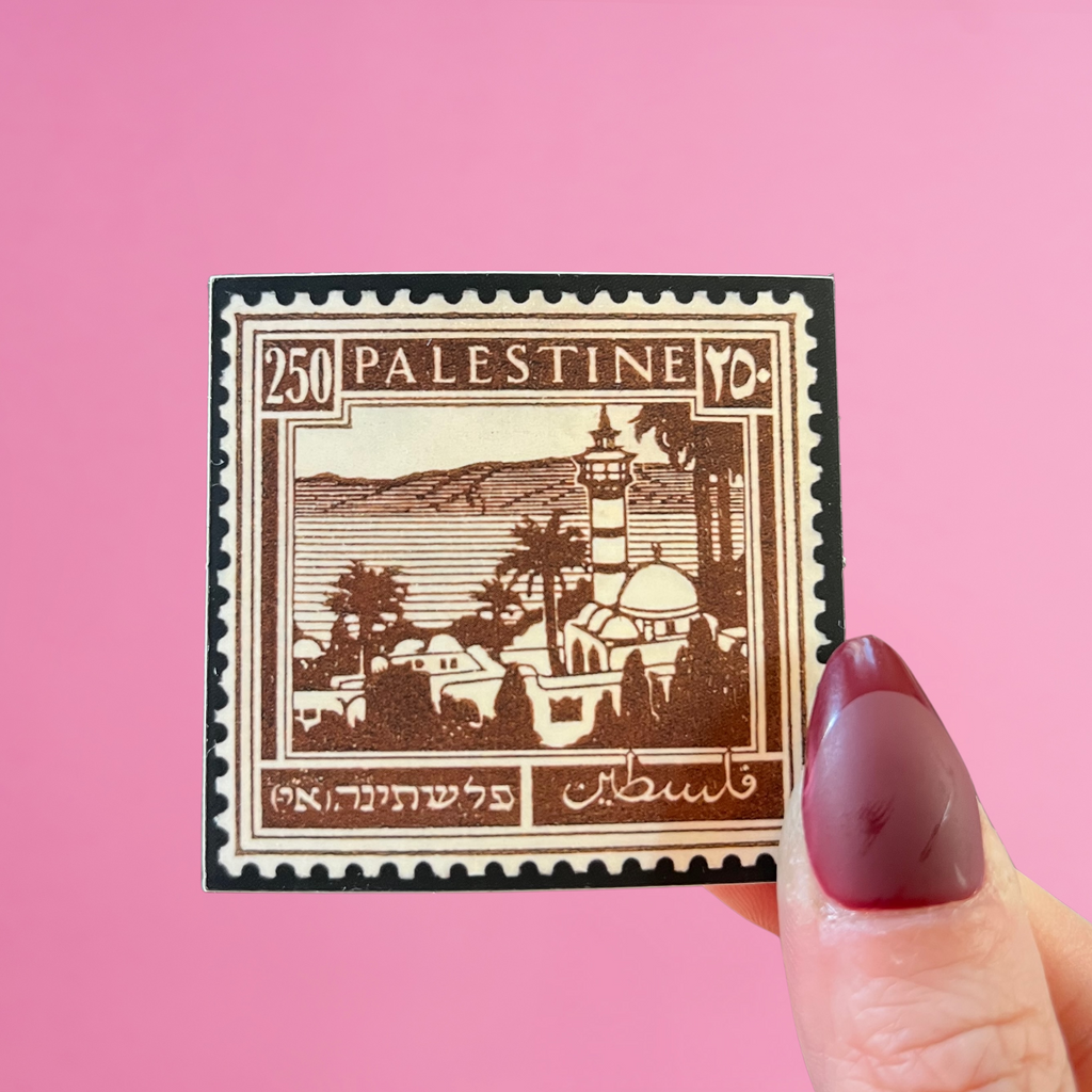 Front view of fingers holding a brown Palestine stamp with an image of Lake Tiberias, at the border of Palestine and Syria. Against a pink background