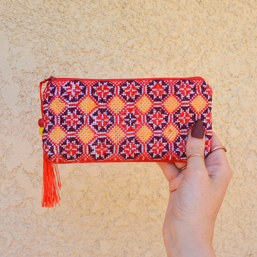 Palestinian tatreez embroidered purse/wallet/clutch bag. red, yellow, and purple star moon design. held by a hand against a off-white wall. view from the front