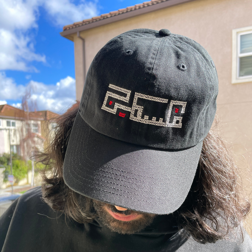 Palestinian embroidered black baseball hat, adjustable and made from 100% Cotton. This hat features an original embroidered design of the word "Palestine" using Arabic Kufic calligraphy. modeled on palestinian man. view from above