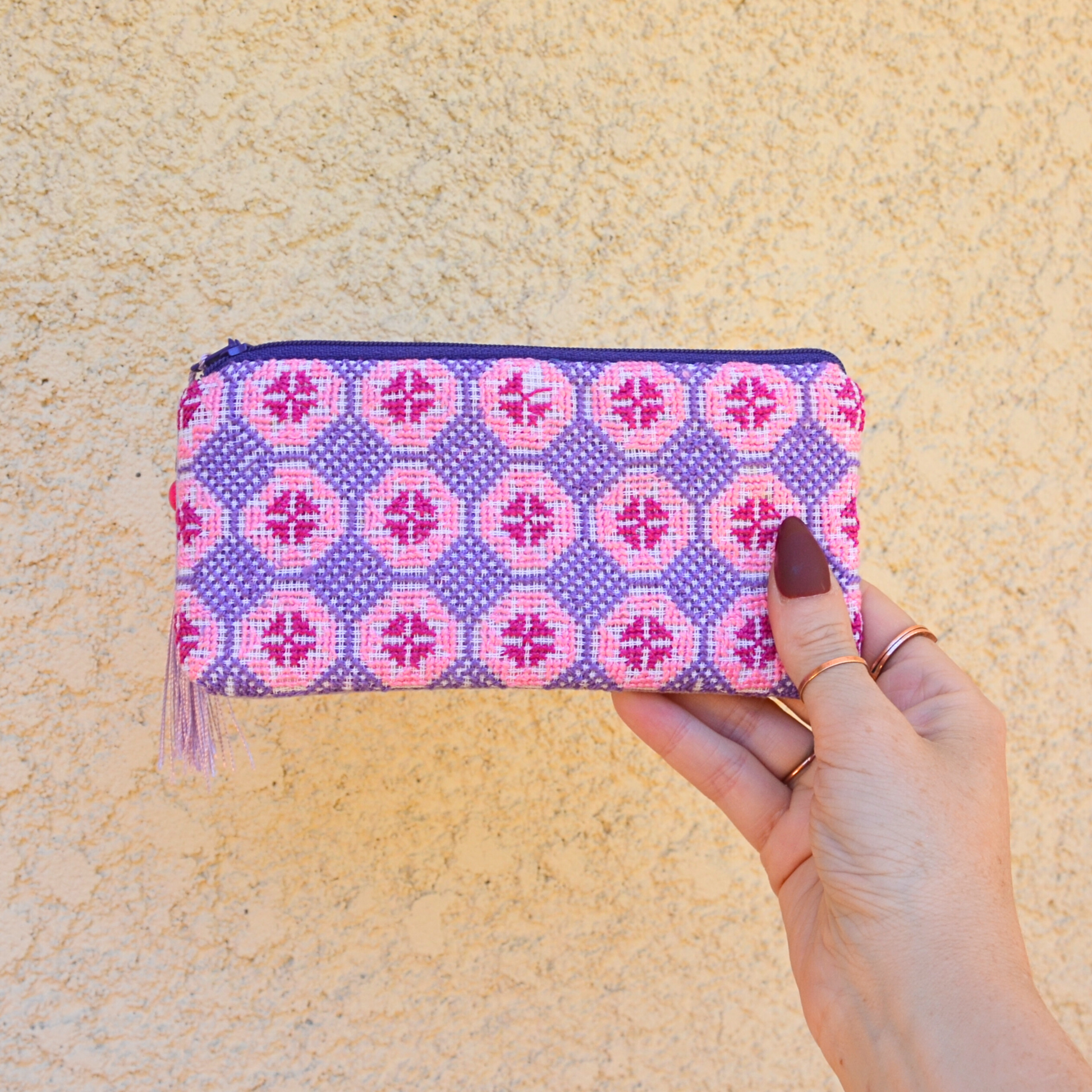Palestinian tatreez embroidered purse/wallet/clutch bag. red, pink, and purple star moon design. held by a hand against a off-white wall. view from the front