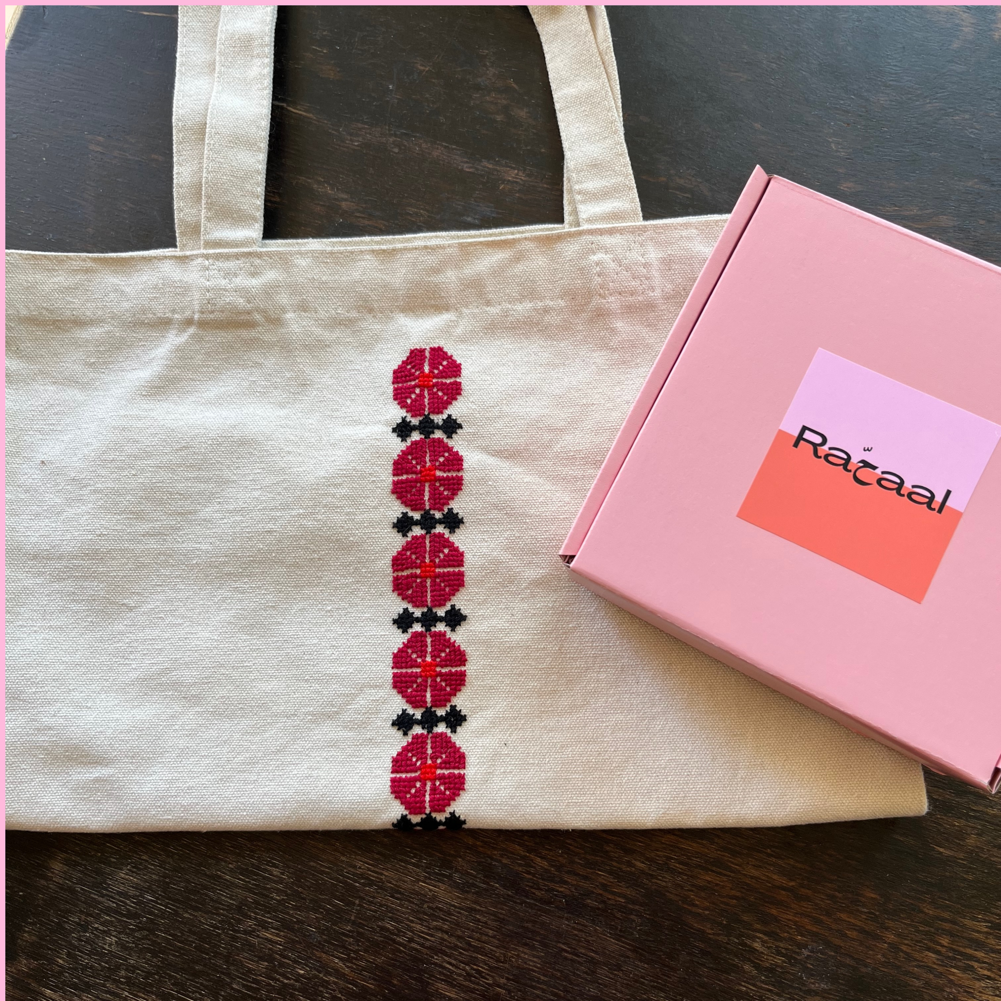 Tatreez tote bag kit with Ramallah flower design. beige tote bag and pink Rahaal tatreez kit box, view from above