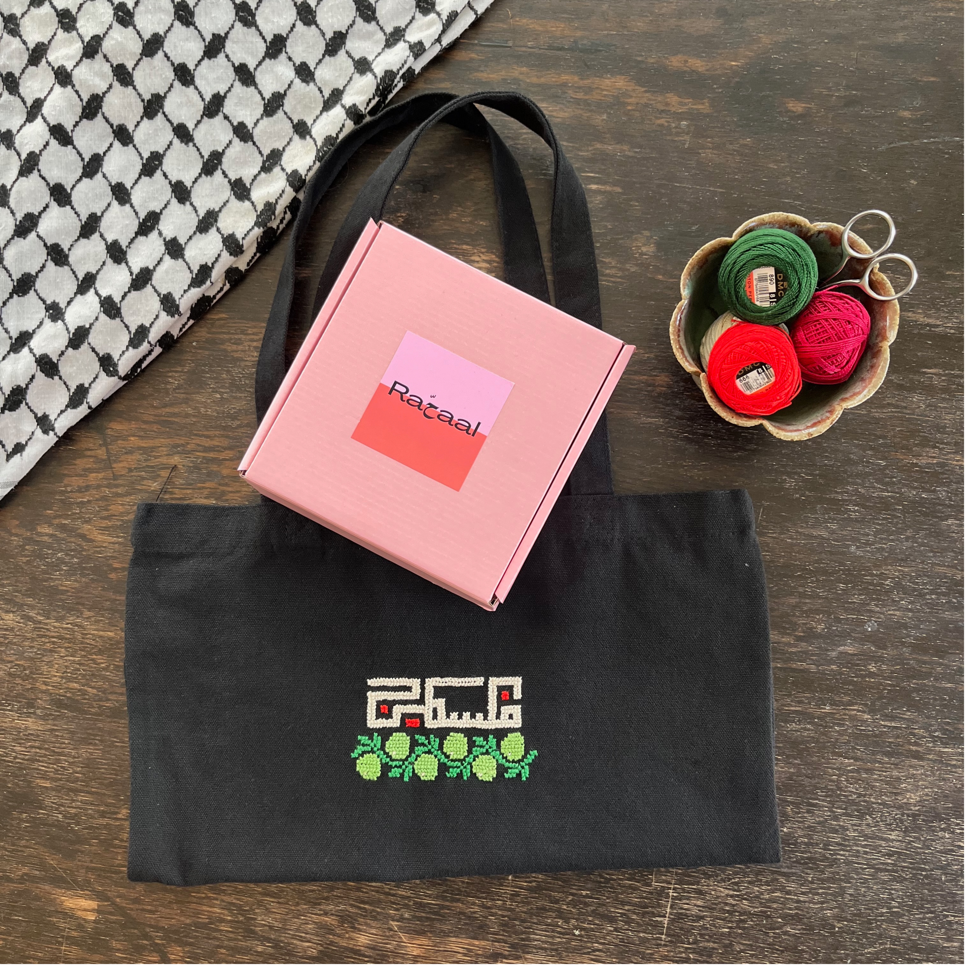 Tatreez tote bag kit with olive branch and Palestine design. black tote bag, pink Rahaal tatreez kit box and embroidery threads, view from above