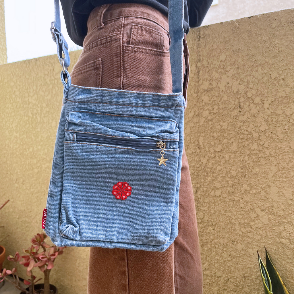 light blue denim purse with handmade tatreez embroidery flower. modeled on woman standing on balcony. view from the front