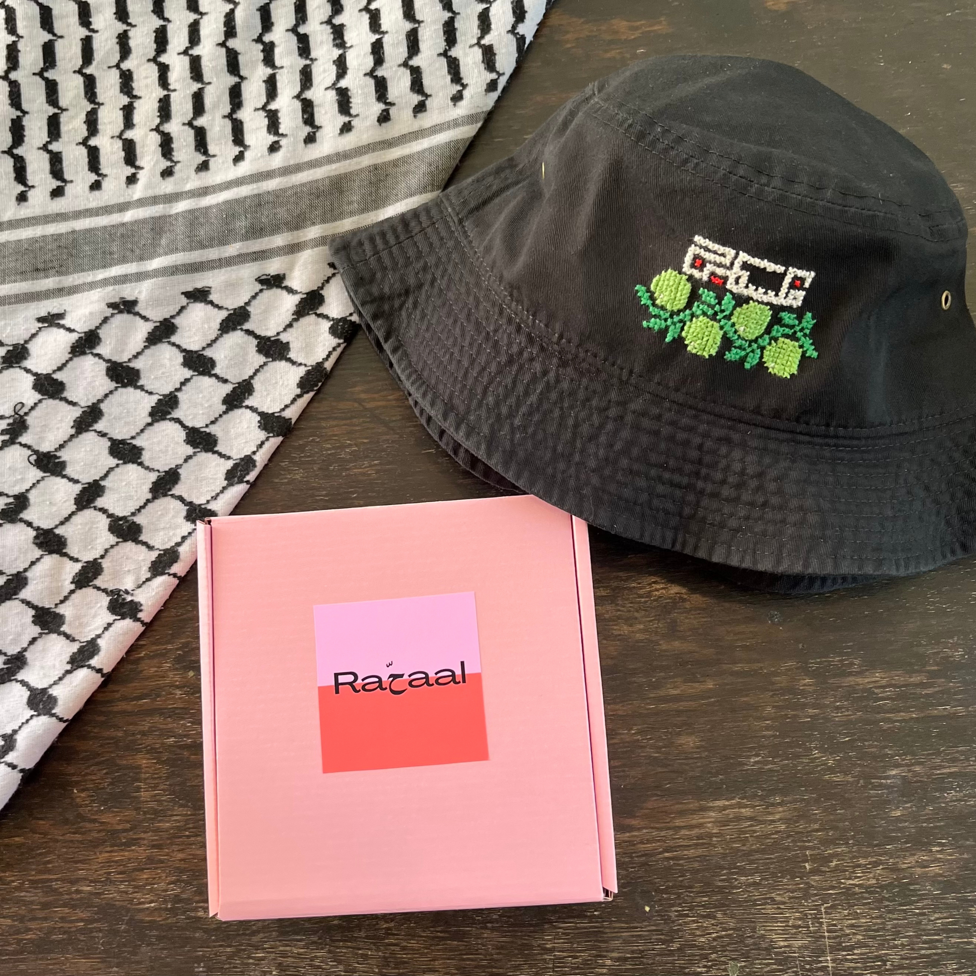 Tatreez bucket hat kit with olive branch and Palestine design. black bucket hat, pink Rahaal tatreez kit box, view from above