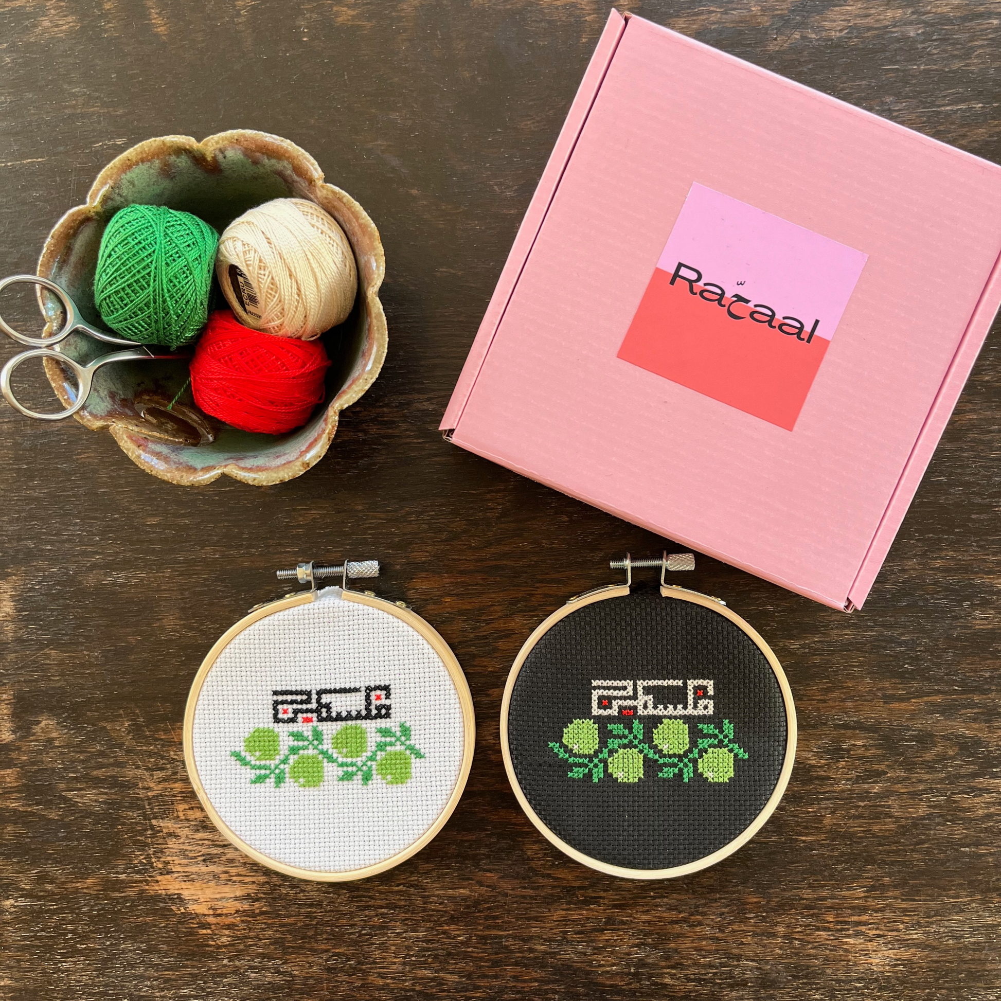 Tatreez kit with olive branch and Palestine design. black aida cloth, embroidery hoop, pink Rahaal tatreez kit box and embroidery threads, view from above