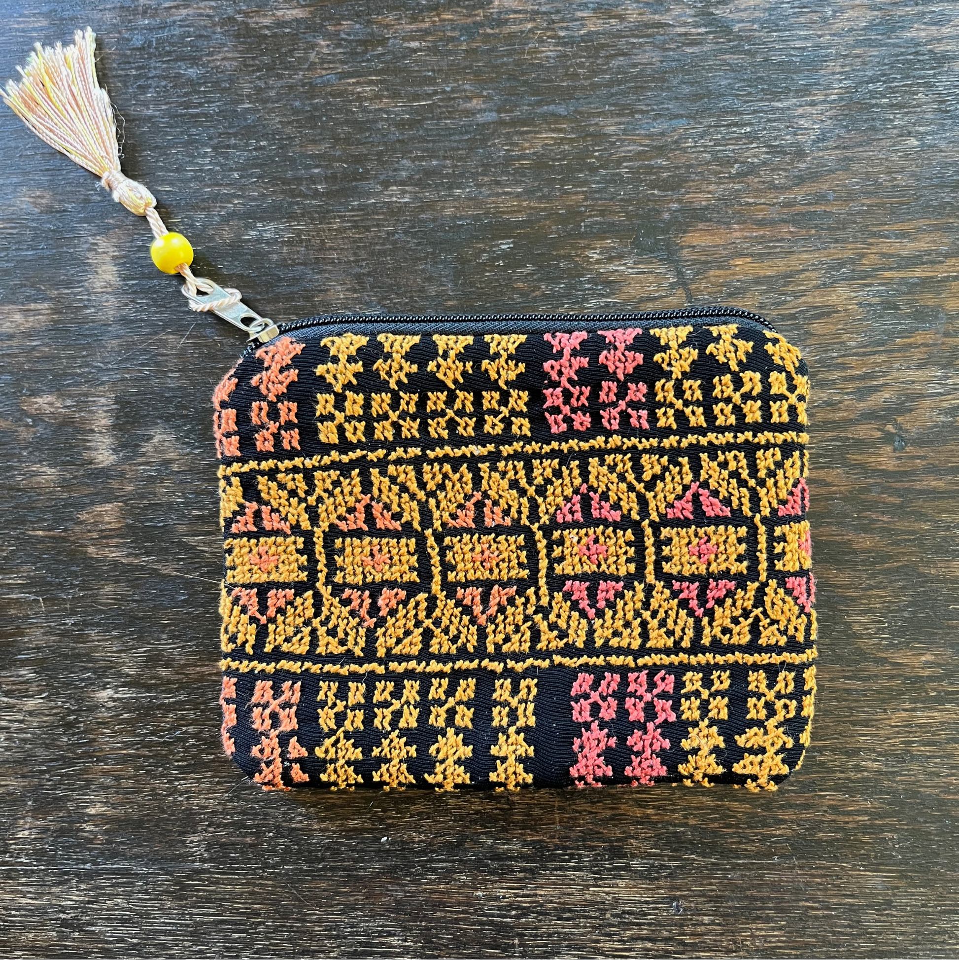 Zippered pouch/wallet with pink and gold handmade Palestinian tatreez embroidery. lying on a wooden table, view from above