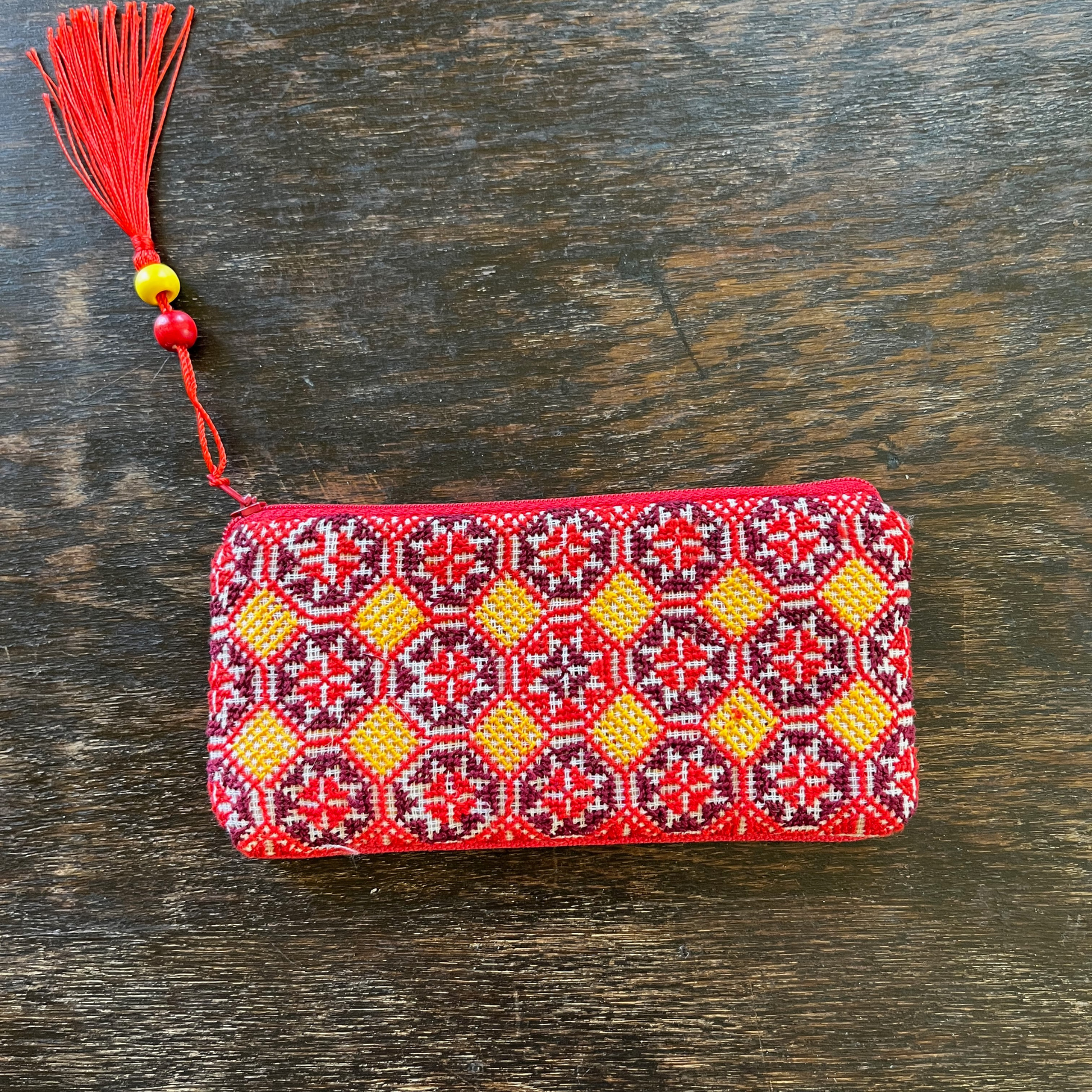 Palestinian tatreez embroidered purse/wallet/clutch bag. red, yellow, and purple star moon design. lying on a wooden table. view from above