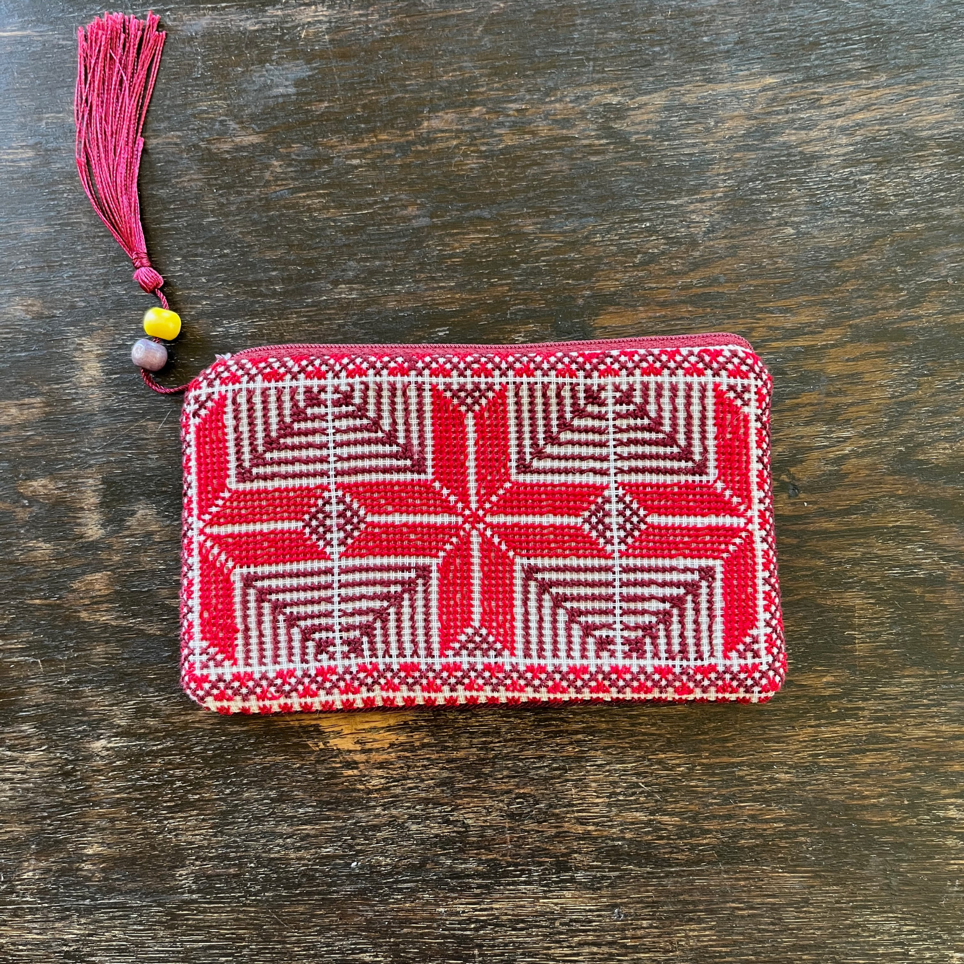 Palestinian tatreez embroidered purse/wallet/clutch bag. red and purple moon with feathers design. lying on a wooden table, view from above