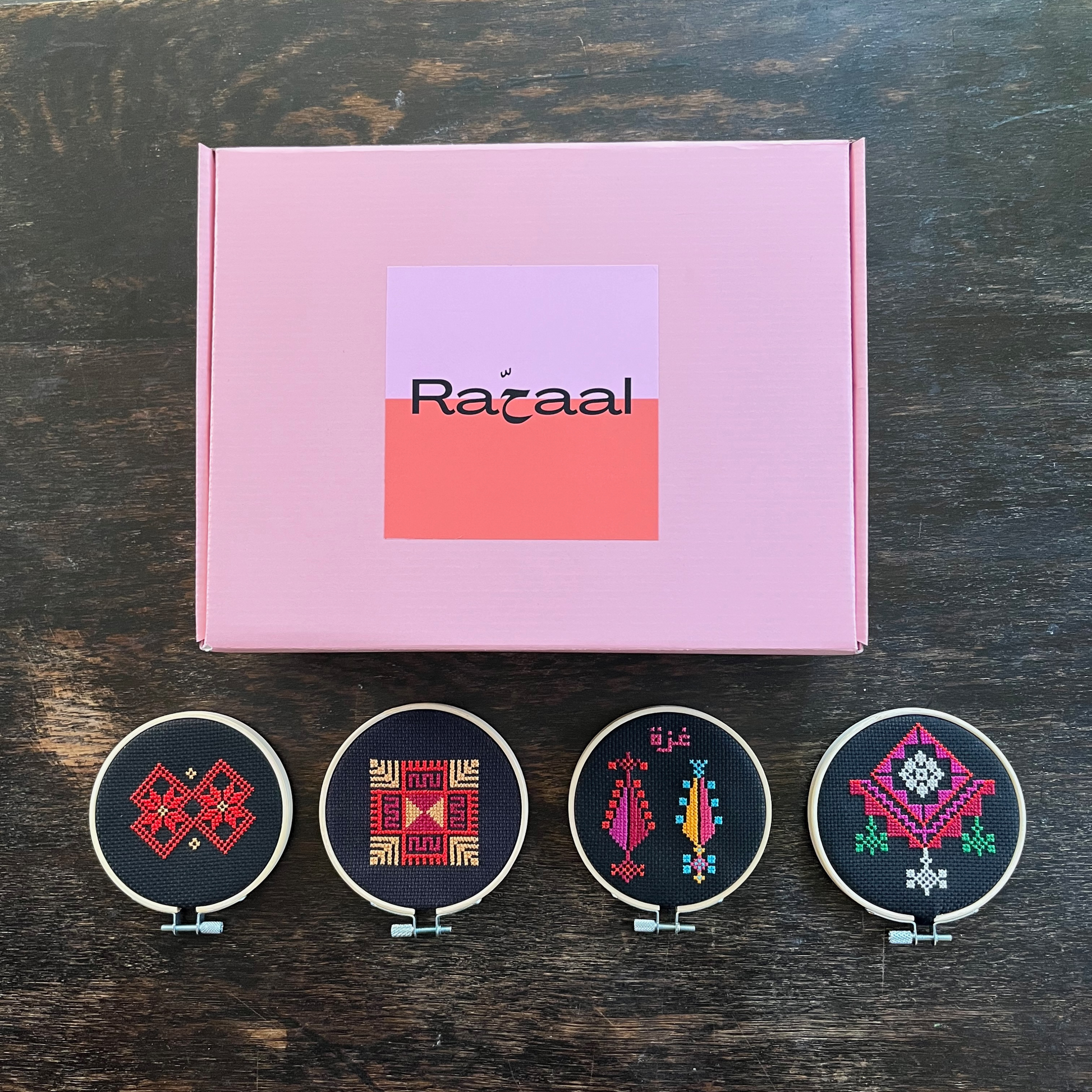 rahaal tatreez workshop kit box with four completed tatreez hoop kits including the al-khalil moon with feathers tatreez kit, the ramallah star moon tatreez kit, the gaza trees tatreez kit, and the al-khalil chandelier tatreez kit. view from above.