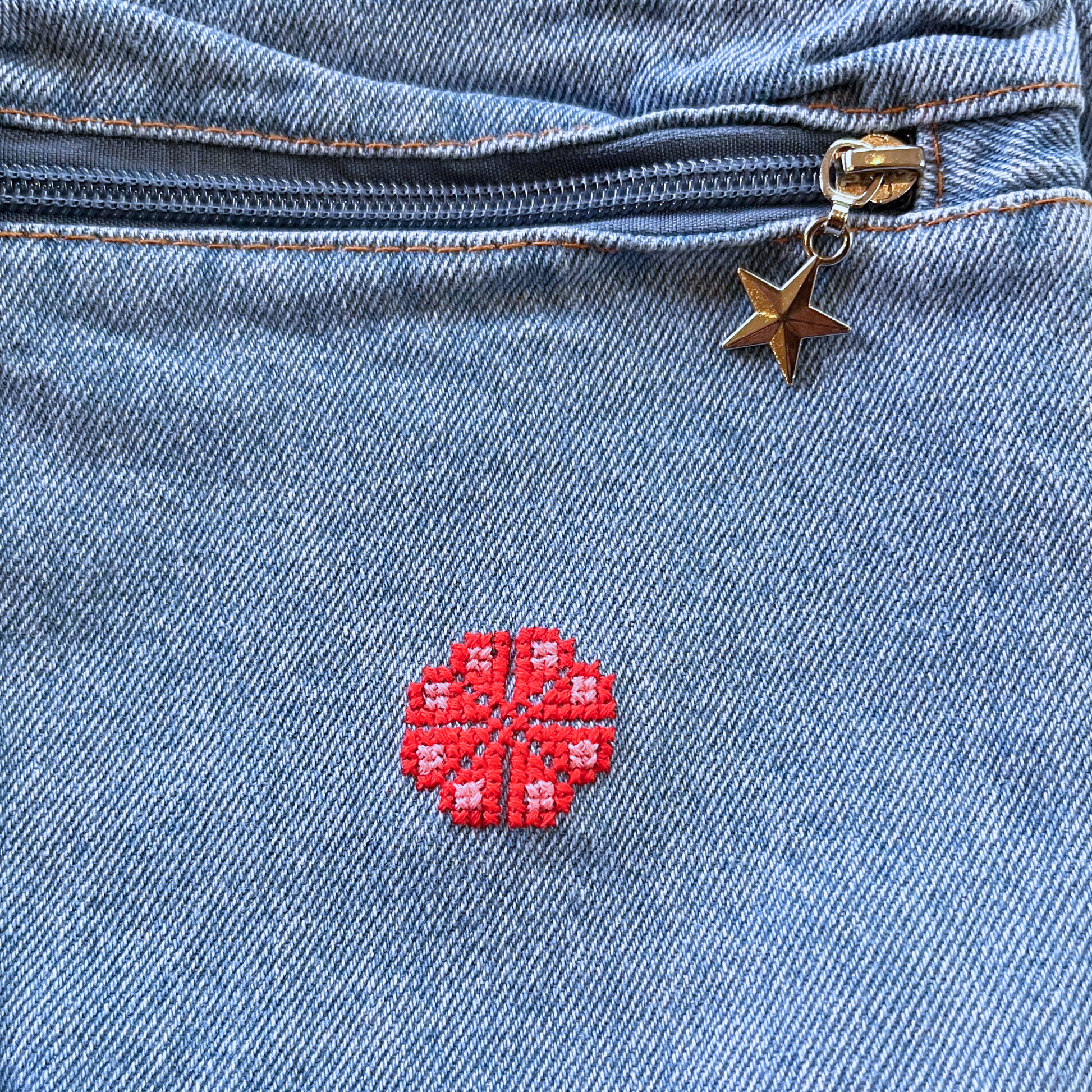 close-up view from above of light blue denim purse with star zipper pull and handmade tatreez embroidery flower.