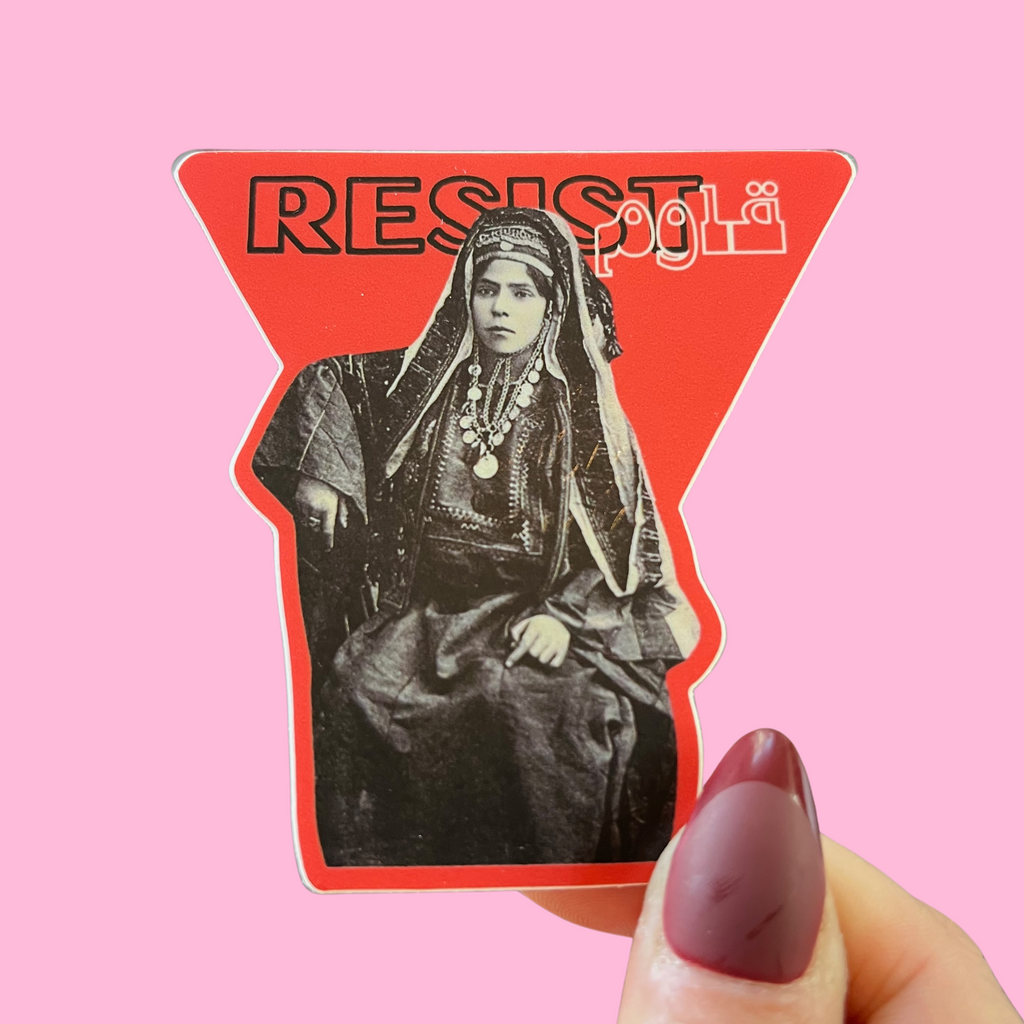 close-up of fingers holding a sticker with an image of a Palestinian woman in traditional dress and the word resist in Arabic and English. against a pink background