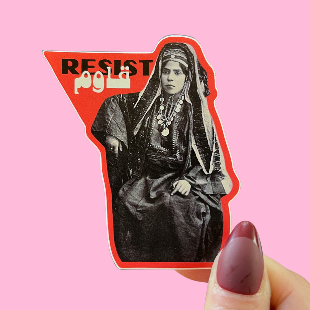 close-up of fingers holding a sticker with an image of a Palestinian woman in traditional dress and the word resist in Arabic and English. against a pink background