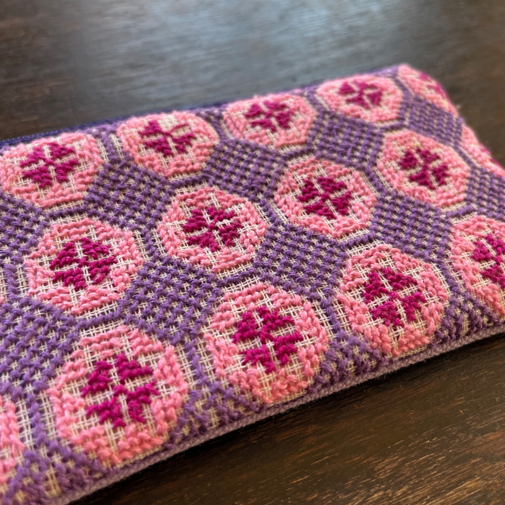 close-up of Palestinian tatreez embroidered purse/wallet/clutch bag. red, pink, and purple star moon design. lying on a wooden table. view from above
