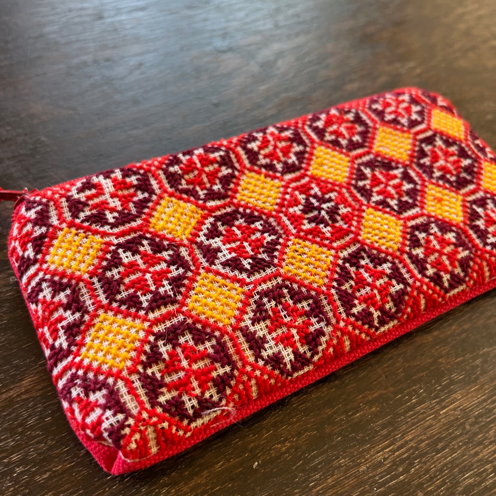 close-up of Palestinian tatreez embroidered purse/wallet/clutch bag. red, yellow, and purple star moon design. lying on a wooden table. view from above