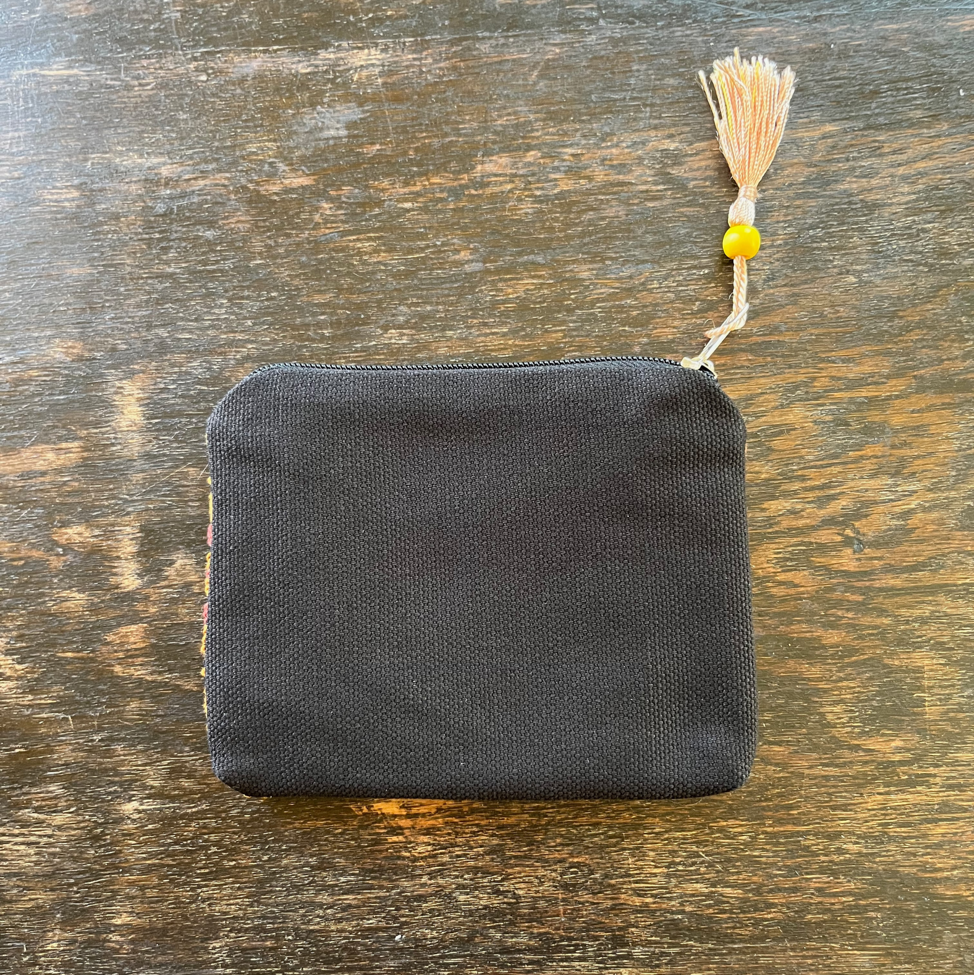 Zippered pouch/wallet with pink and gold handmade Palestinian tatreez embroidery. lying on a wooden table, view of the backside from above