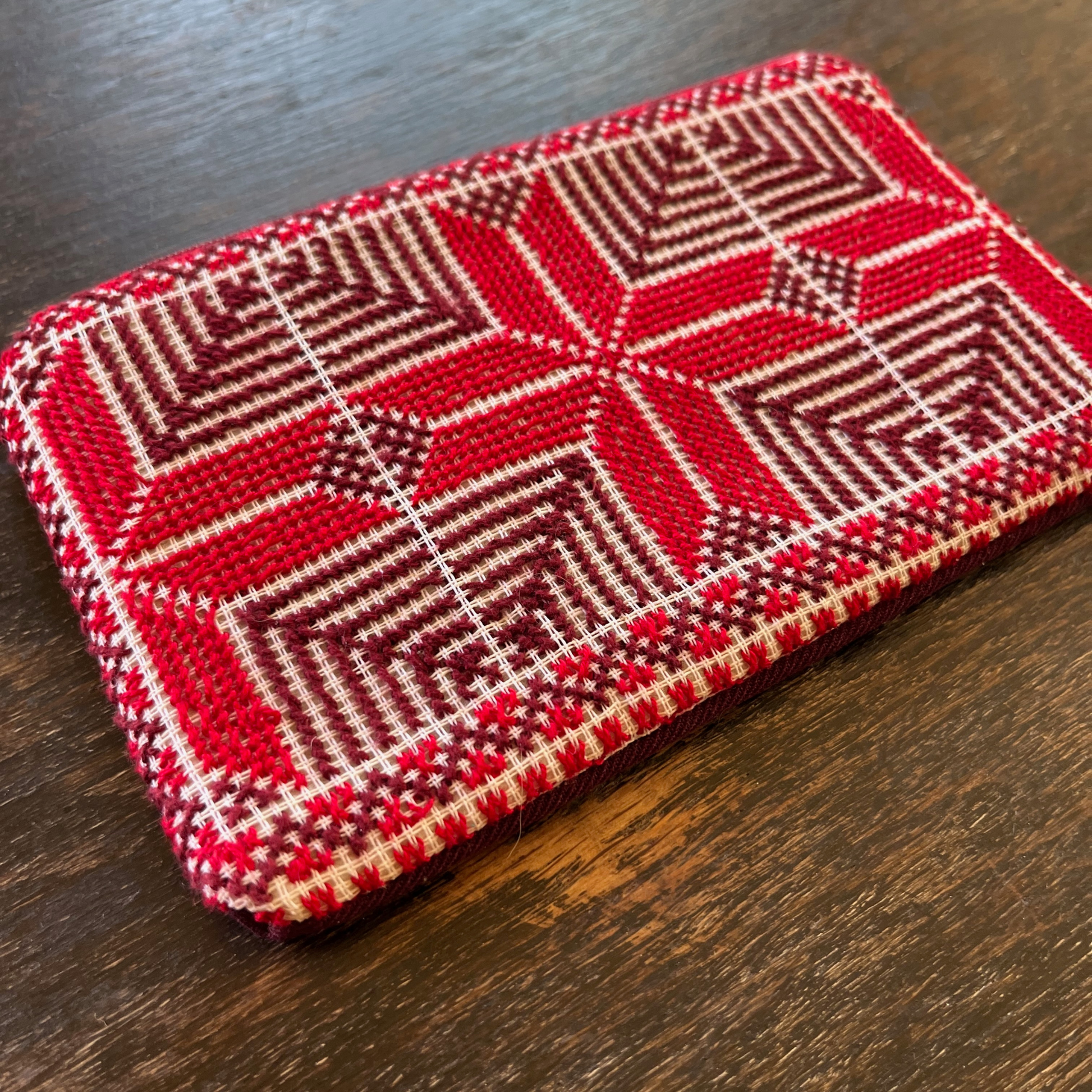 close-up of Palestinian tatreez embroidered purse/wallet/clutch bag. red and purple moon with feathers design. lying on a wooden table, view from above