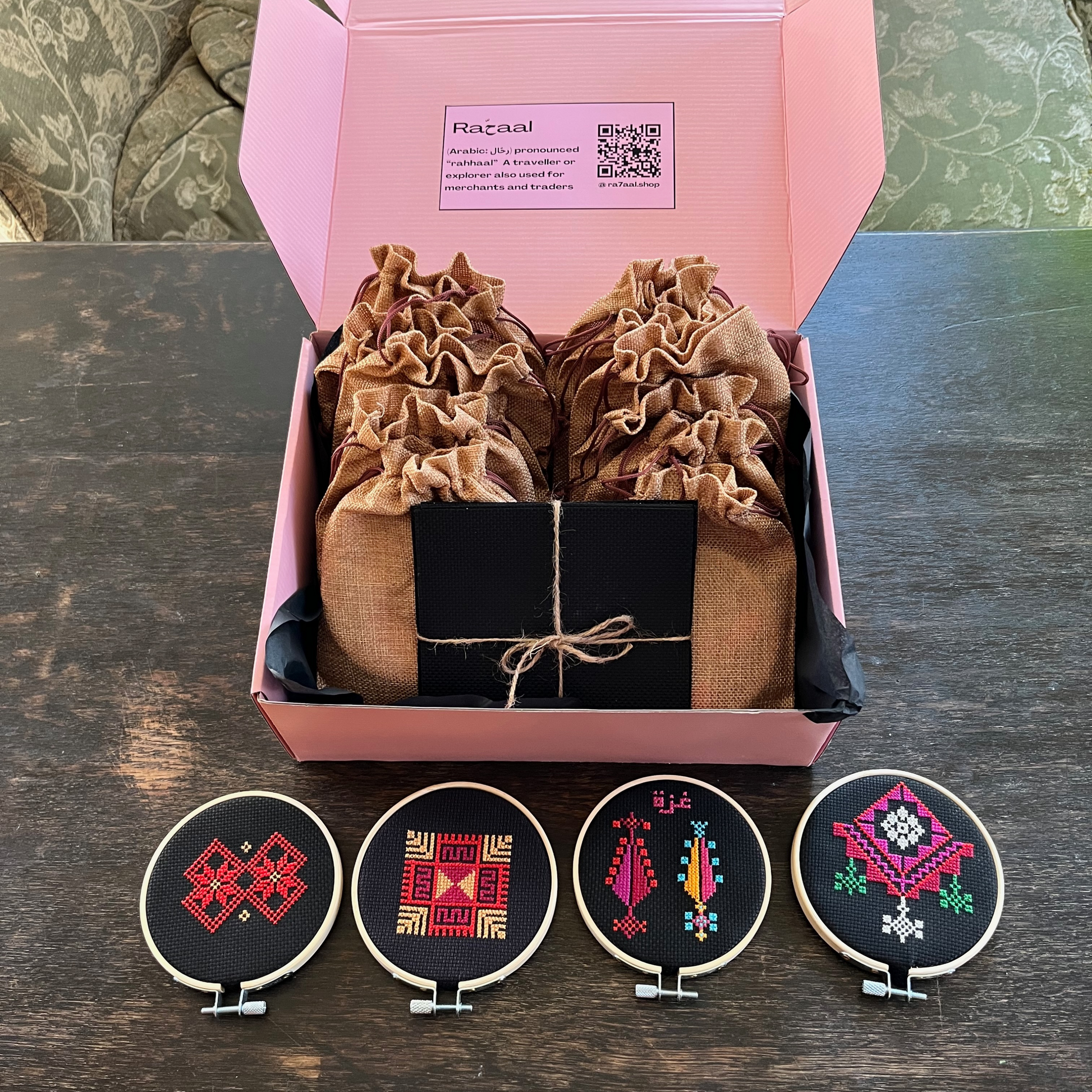 rahaal tatreez workshop kit box with four completed tatreez hoop kits including the al-khalil moon with feathers tatreez kit, the ramallah star moon tatreez kit, the gaza trees tatreez kit, and the al-khalil chandelier tatreez kit. view from above.