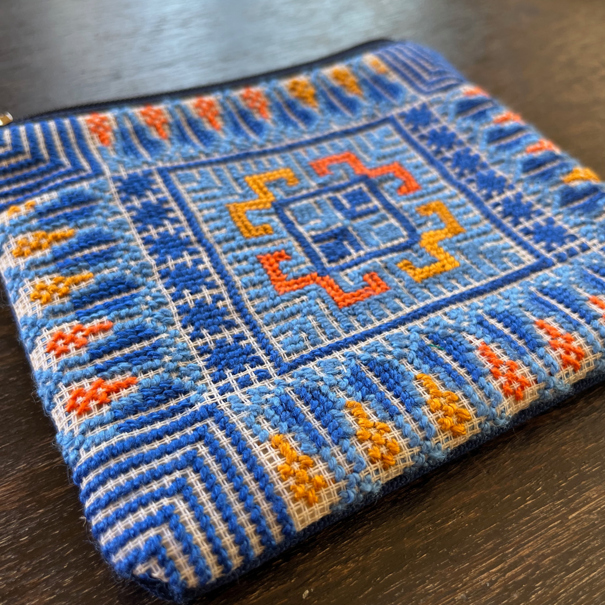 close-up of Palestinian tatreez embroidered purse/wallet/clutch bag. blue and orange cypress tree and moon with feathers design. lying on a wooden table view from above