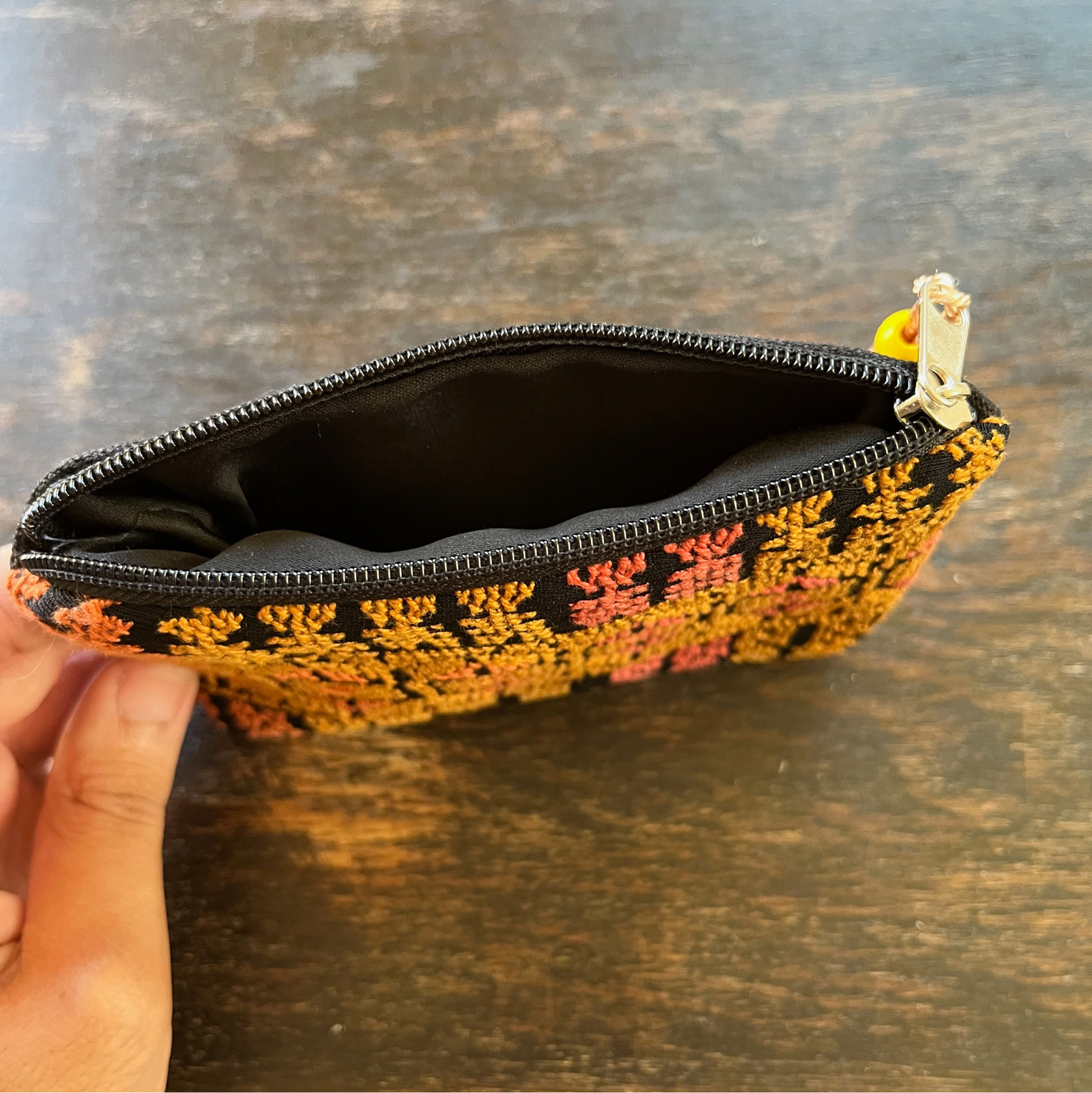 Zippered pouch/wallet with pink and gold handmade Palestinian tatreez embroidery. standing on a wooden table, view of the interior from above