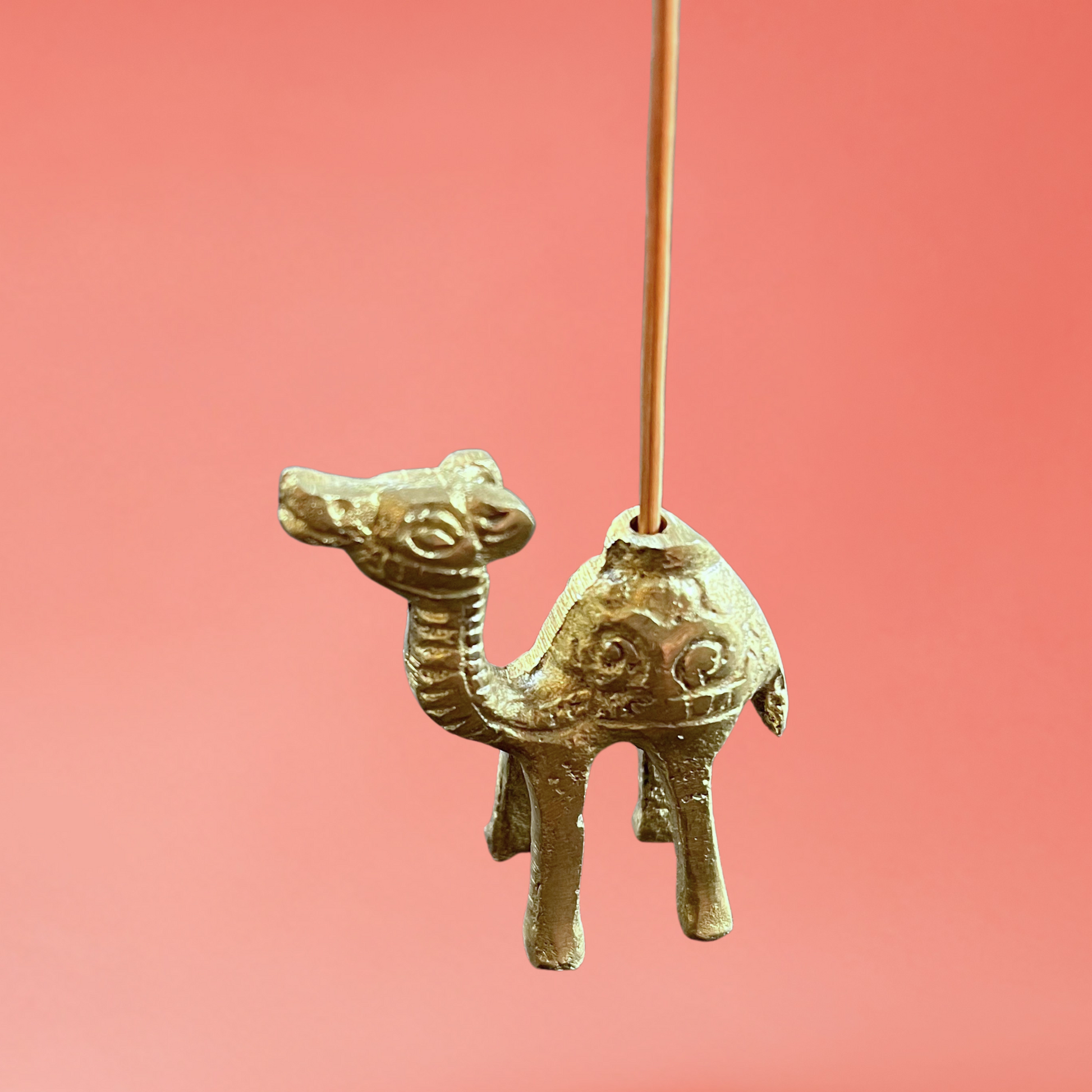 brass, gold camel incense holder, side view on pink background