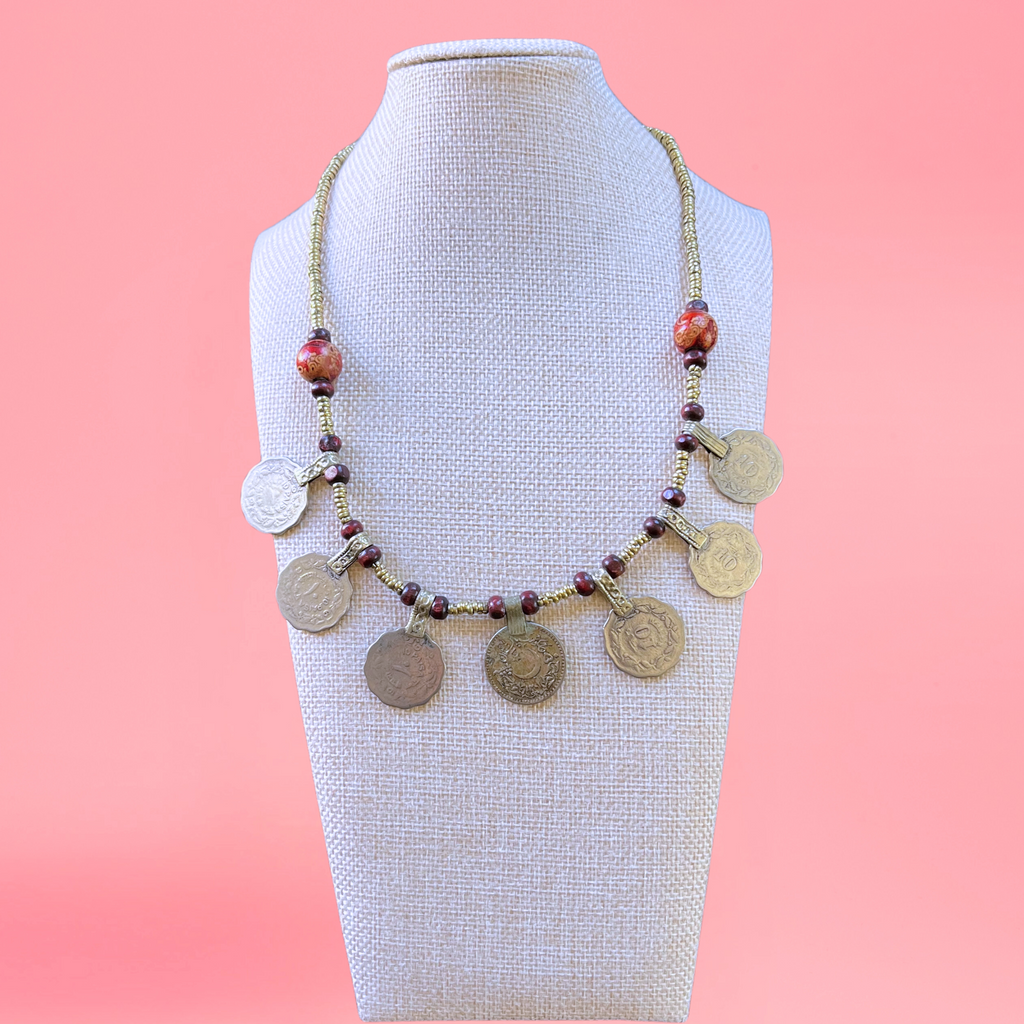necklace modeled on a beige bust with a pink background. Necklace features turkish coins, metal beads, and wooden beads. view from the front