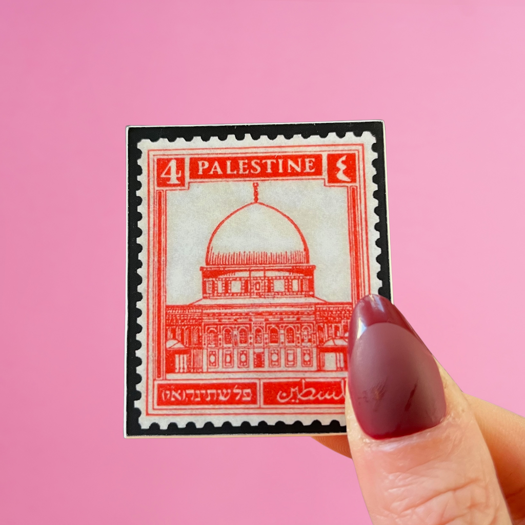 Front view of fingers holding a Palestine stamp with an image of the dome of the rock in jerusalem. Against a pink background