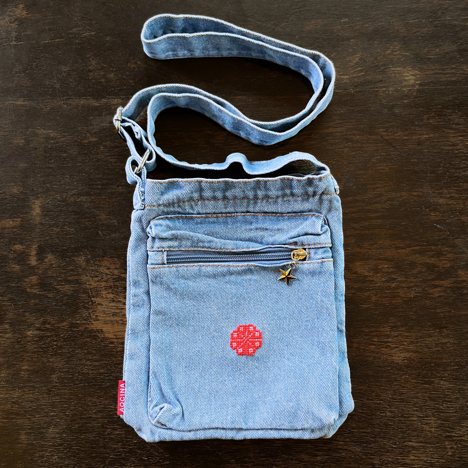 light blue denim purse with handmade palestinian tatreez embroidery flower on wooden background. view from above