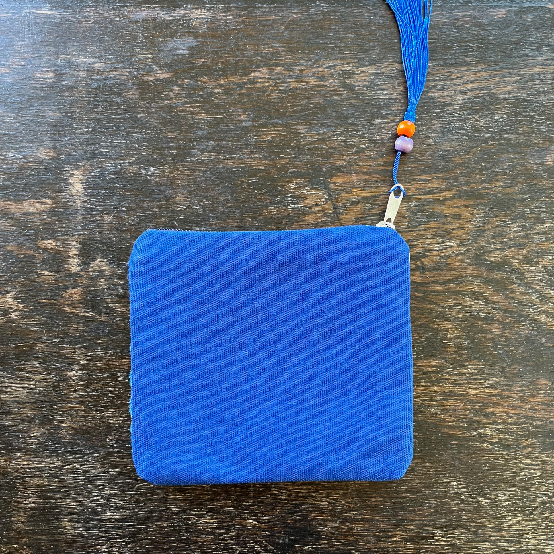 Palestinian tatreez embroidered purse/wallet/clutch bag. blue and orange cypress tree and moon with feathers design. lying on a wooden table view from above