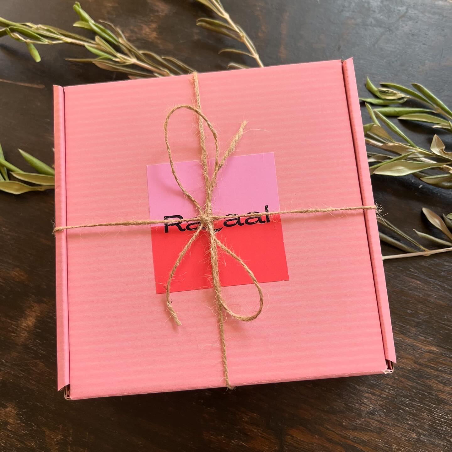 Rahaal pink tatreez kit box, tied with twine, on top of an olive branch. view from above