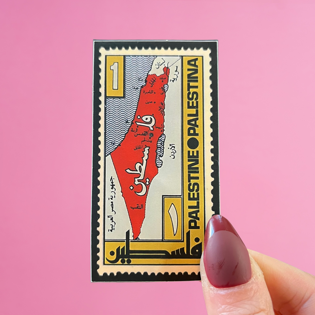 Front view of fingers holding a Lebanon stamp with a palestine map. Against a pink background