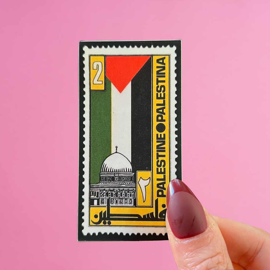 Front view of fingers holding a Lebanon stamp with a palestine flag and the dome of the rock in jerusalem. Against a pink background