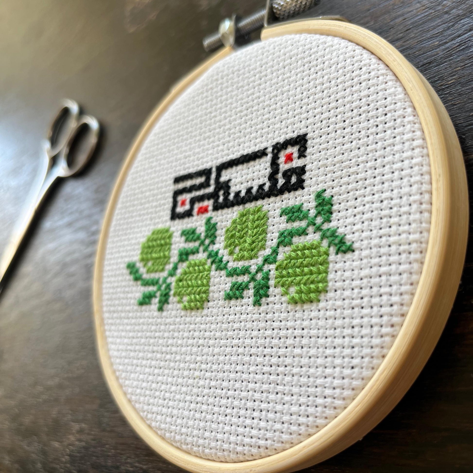 Tatreez kit with olive branch and Palestine design. white aida cloth in embroidery hoop next to embroidery scissors. view from the side