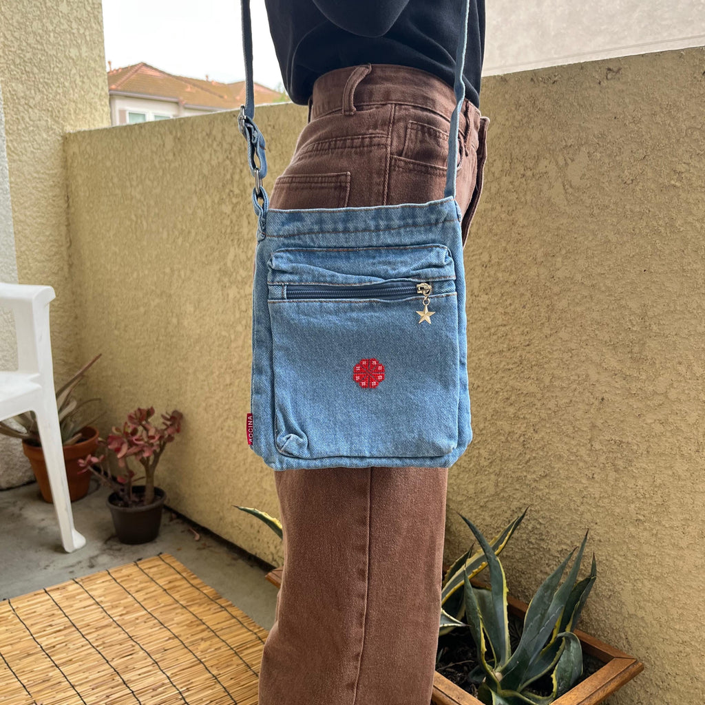 light blue denim purse with handmade tatreez embroidery flower. modeled on woman standing on balcony. view from the front