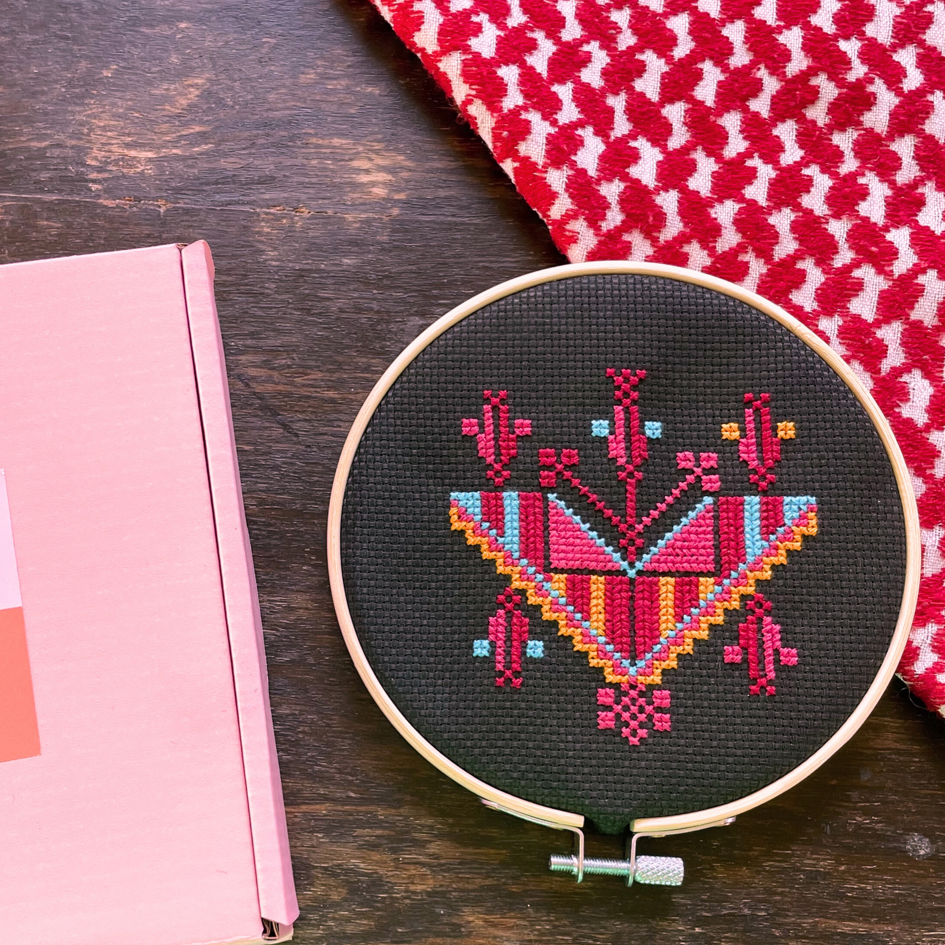 Tatreez kit with Gaza necklace design. black aida cloth, embroidery hoop, pink Rahaal tatreez kit box, view from above