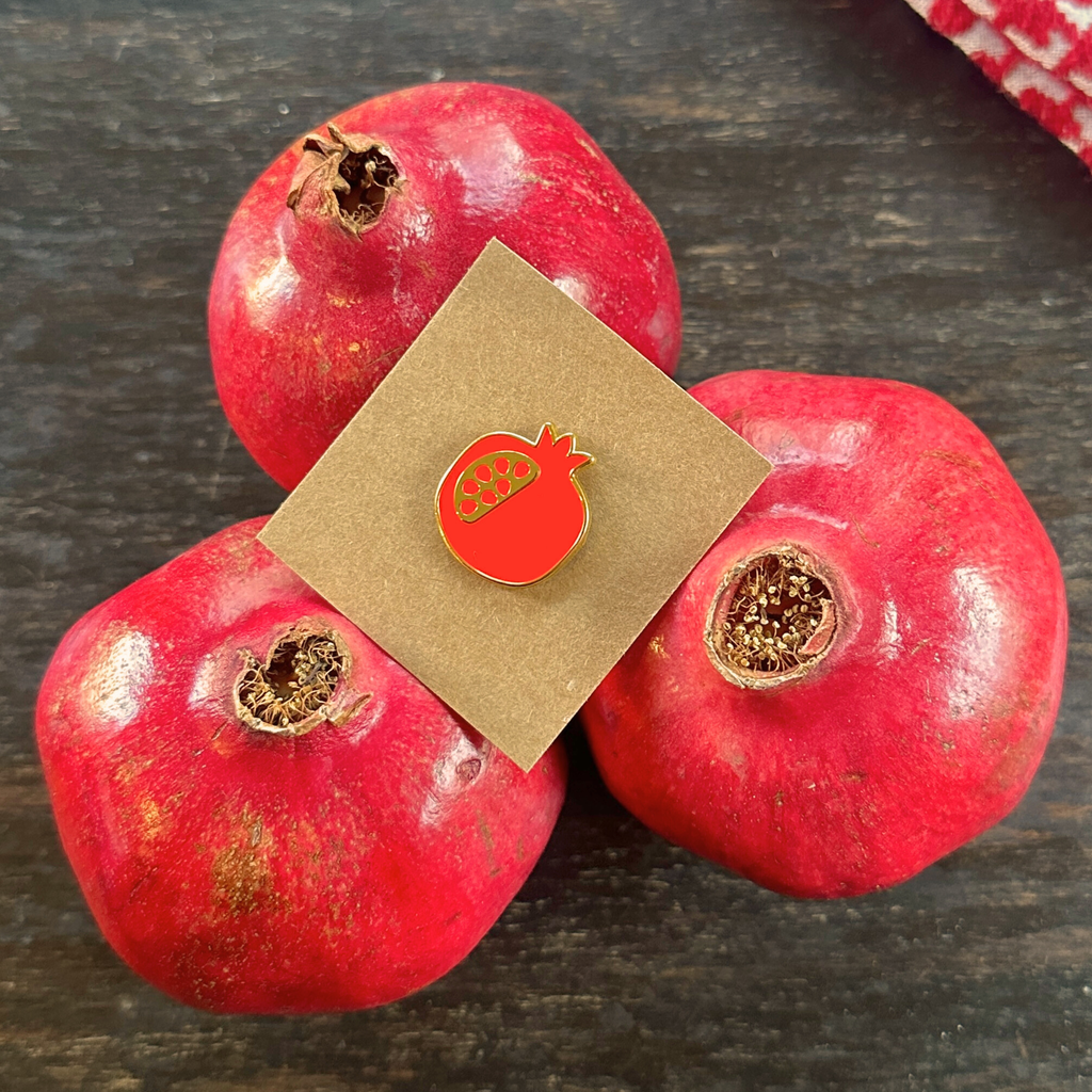A red pomegranate needle minder enamel pin with gold edging. Cute birthday gift for artsy friend. gift under $20
