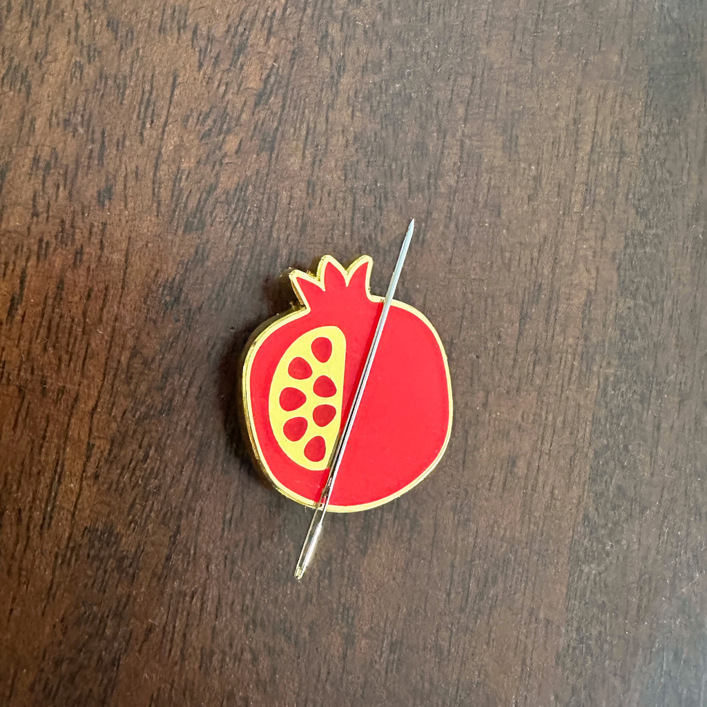 A red pomegranate needle minder enamel pin with gold edging. Cute birthday gift for artsy friend. gift under $20